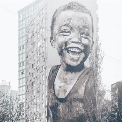 A large image of a young child, smiling at something in the distance, painted against a very tall block of residential flats on a foggy day with trees in the foreground